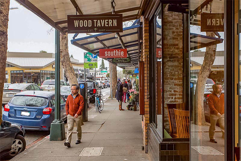 People walking down a sidewalk with an awning over it that displays signage for all the storefronts