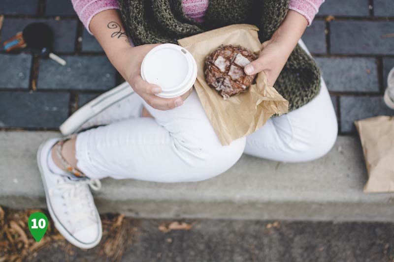 A woman holds a pasty and a cup of coffee