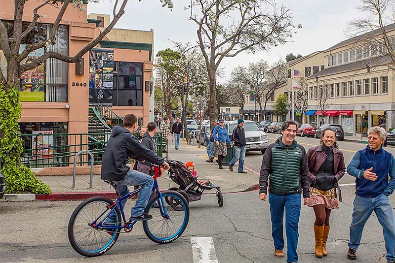 A cyclist rides through a group of people walking down the street in Rockridge, Oakland