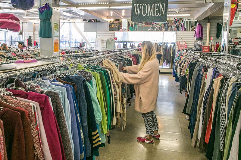 A woman looking through packed clothing racks indoors at a thrift store in San Francisco