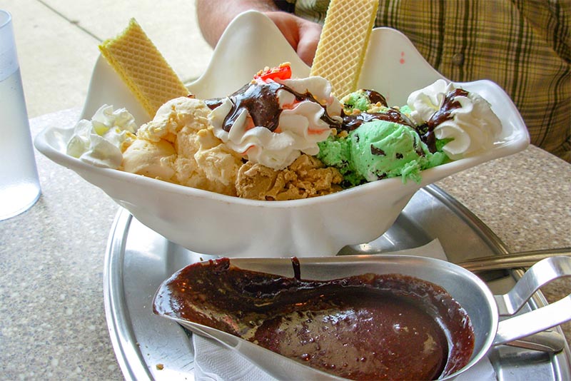 A large ice cream sundae in a shell-shaped bowl with a side of chocolate sauce from Margie's Candies in Chicago