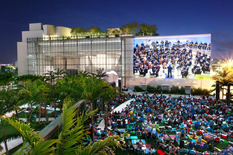 Crowds of people attending teh outdoor showing of the New World Symphony concert. 