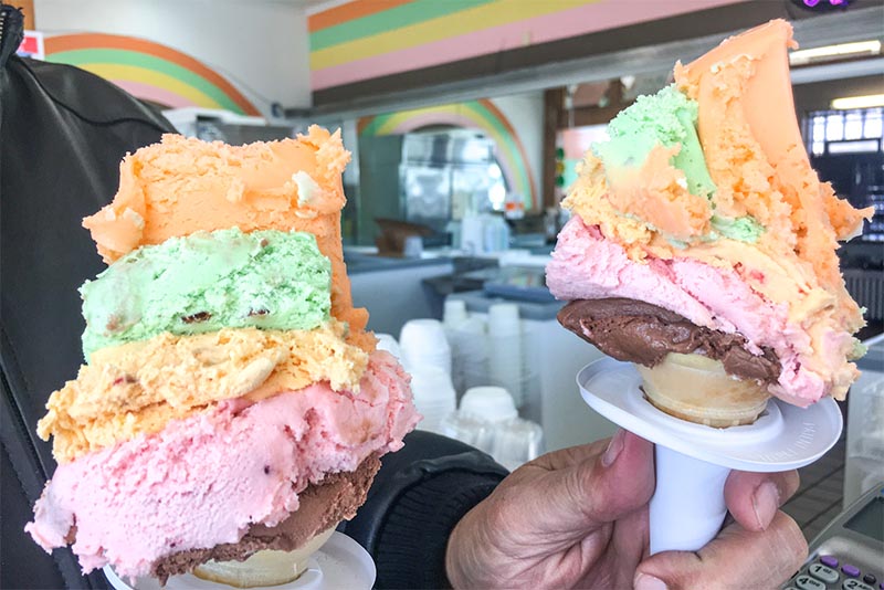 A person holds two Chicago Rainbow Cones of multi-colored ice cream