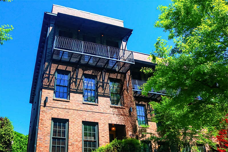 An upward view of a brick condominium building with a balcony against a blue sky