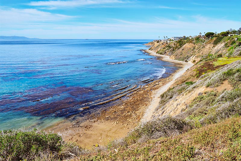 Grassy hills overlook a small beach near crystal blue waters in the Los Angeles area