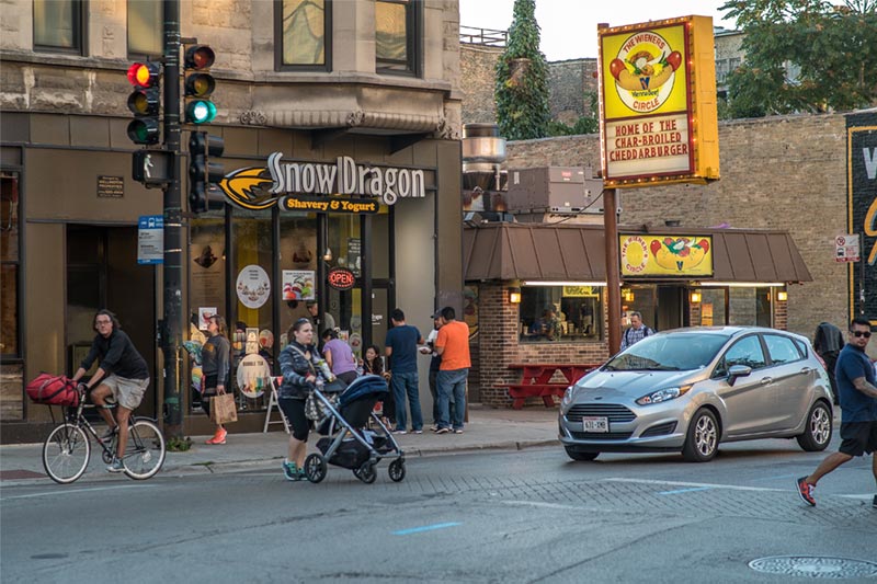 woman with stroller walking across neighborhood intersection in front of businesses