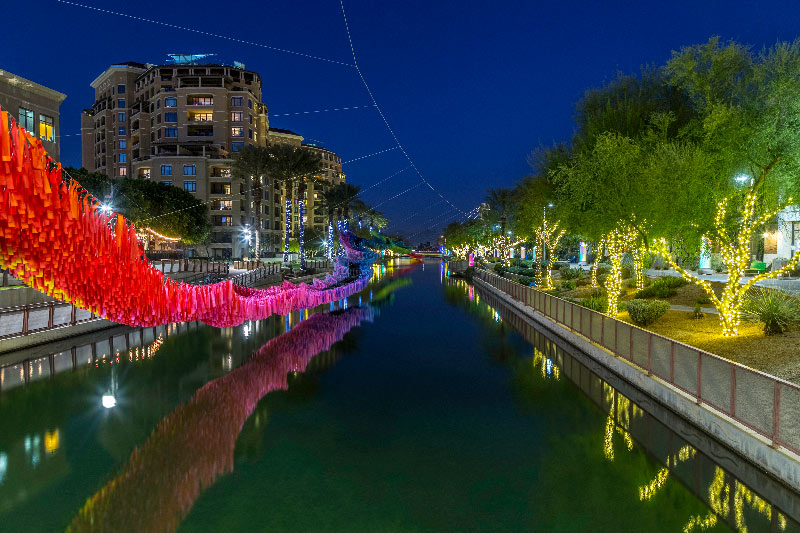 Scottsdale canal at night with colorful art sculpture hanging over the water with apartments in background.