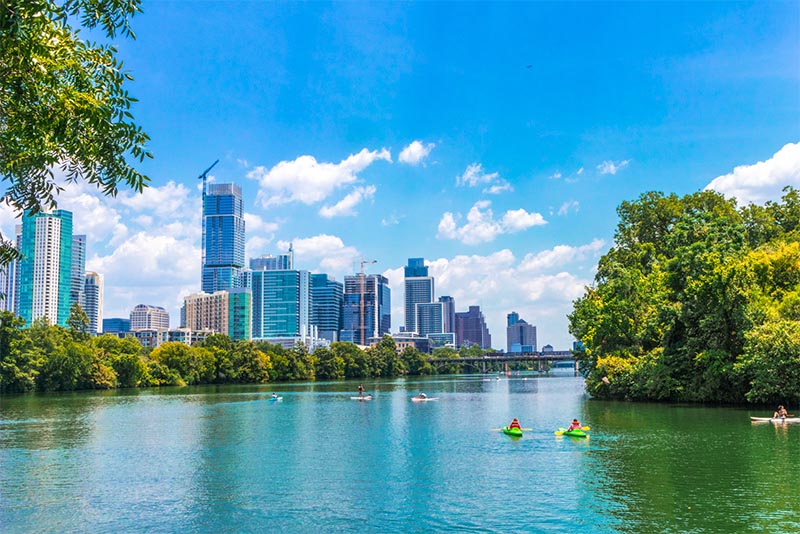 People kayak in the Colorado River with Austin buildings rising up in front of them