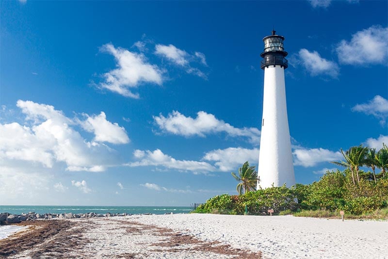 A lighthouse rises above the beach and blue water of Bill Baggs Cape Florida State Park