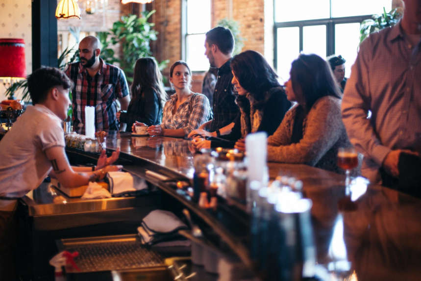 A busy bar with bartender making drinks for customers.