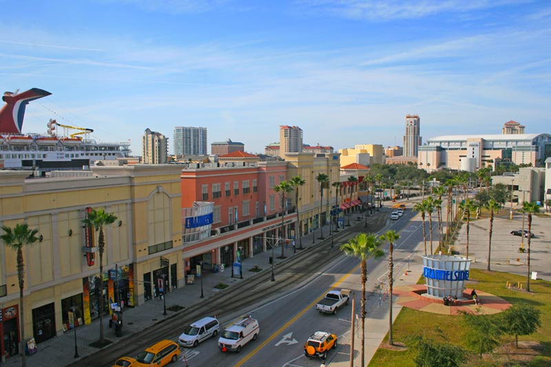 Aerial view of neighborhood buildings and cars along street with skyline in the distance.