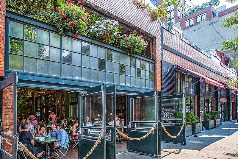 A restaurant in Chelsea New York City with its doors open where you can see patrons inside