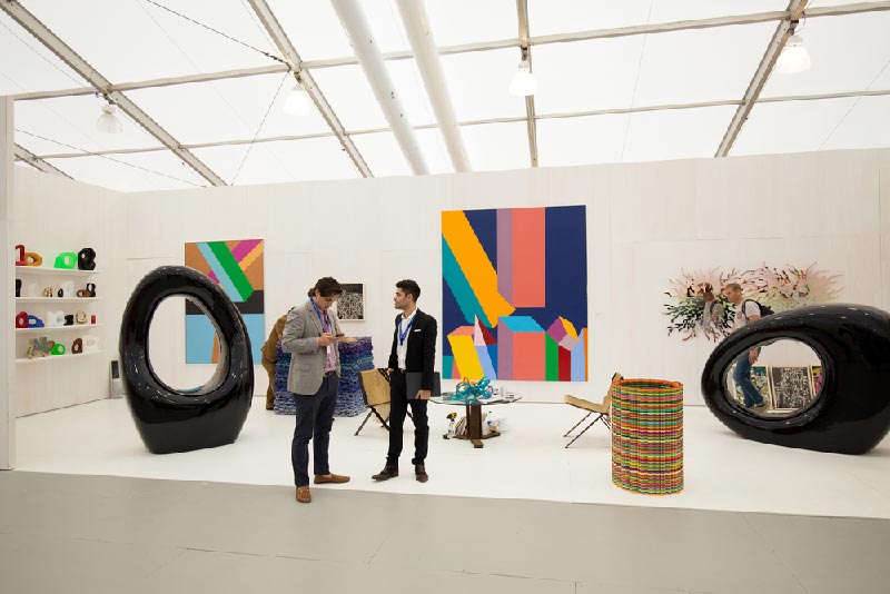 People walking around all white art museum with colorful sculptures in the middle.