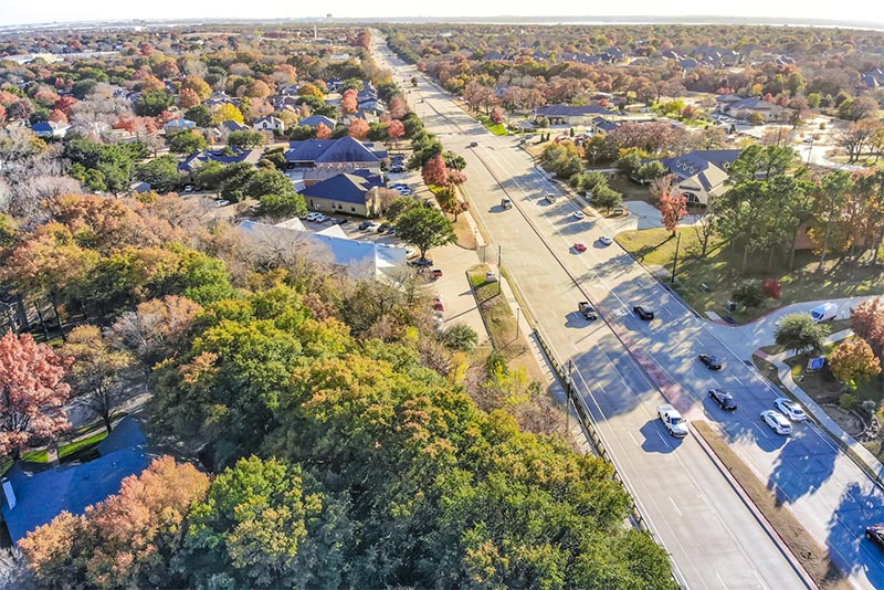 An aerial view of a highway in Dallas, with many homes and trees also pictured