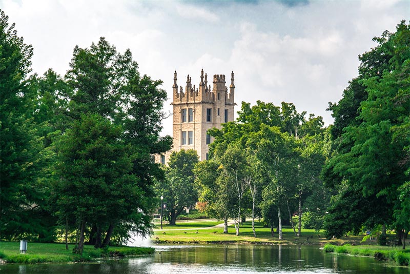 A castle-like building at Northern Illinois University rises above green trees in DeKalb
