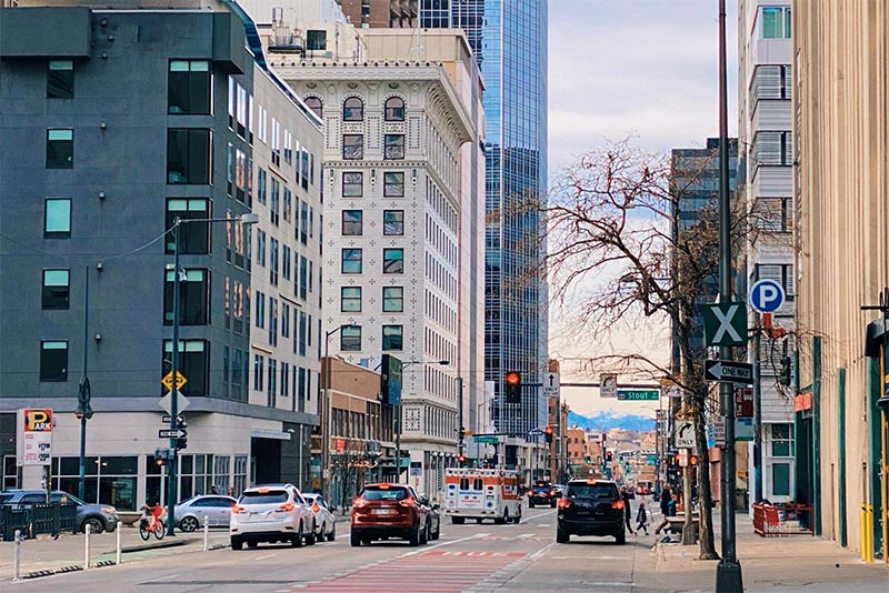 A downtown Denver streetscape with cars in the road and tall buildings surrounding