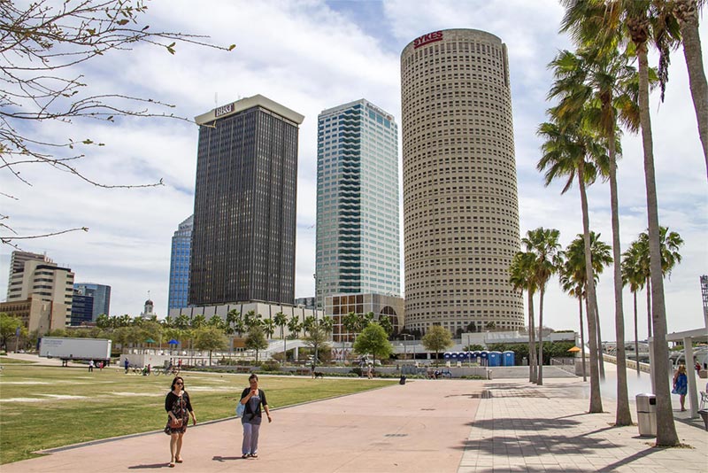 People walking in park with high rise buildings in background.