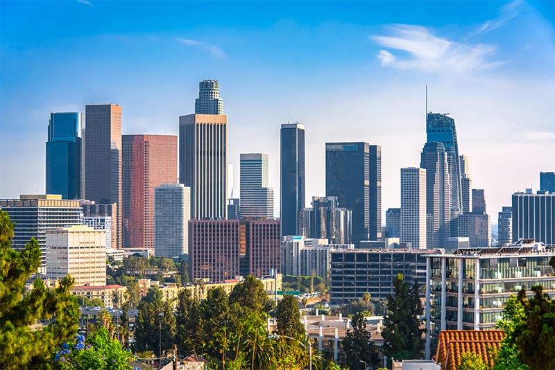 The skyline of Downtown Los Angeles rising above trees and houses with a blue sky above