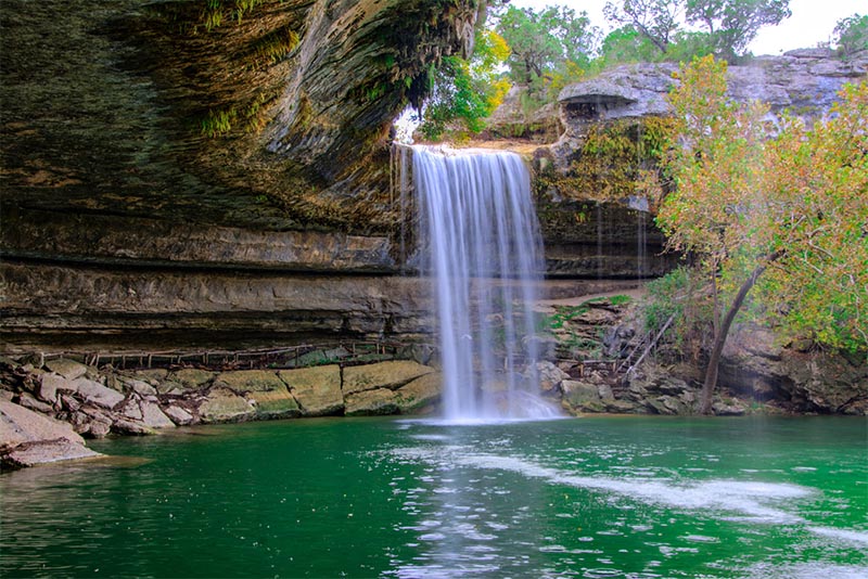 A waterfall falls into a basin from a semi-circle of light at the top of a rock wall