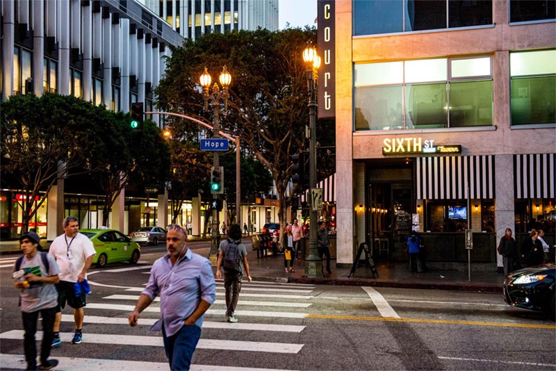 Pedestrians crossing downtown street with bar in background.