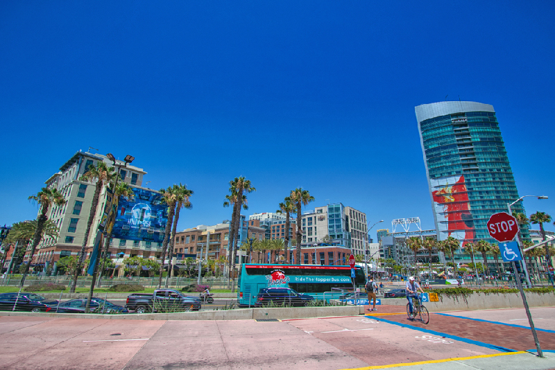 View of bus leaving bus stop in front of park and San Diego skyline.