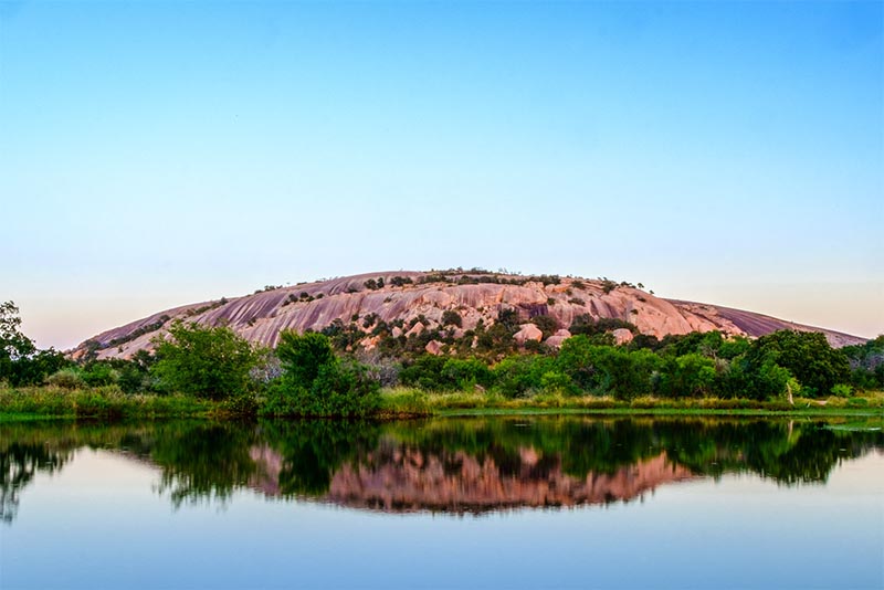 Enchanted Rock, a large round rock formation in Texas, emerges from the ground surrounded by grass