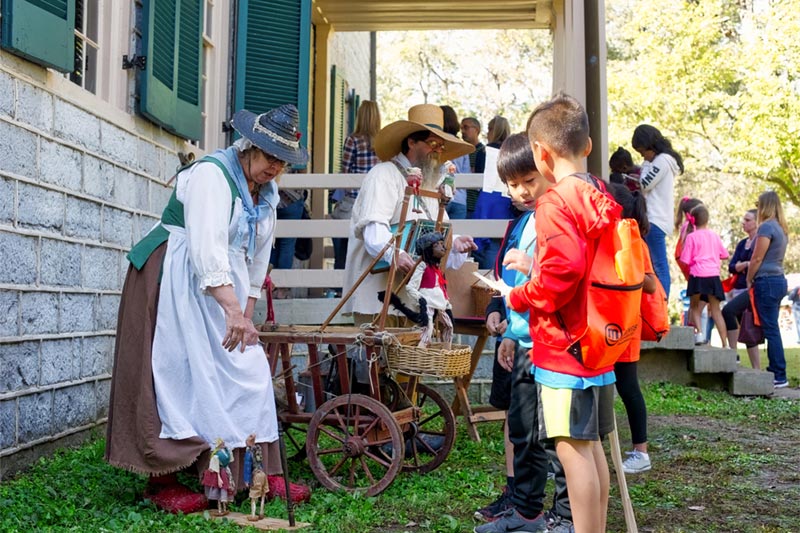 Kids gathered around woman showcasing water gathering by home with people in background.