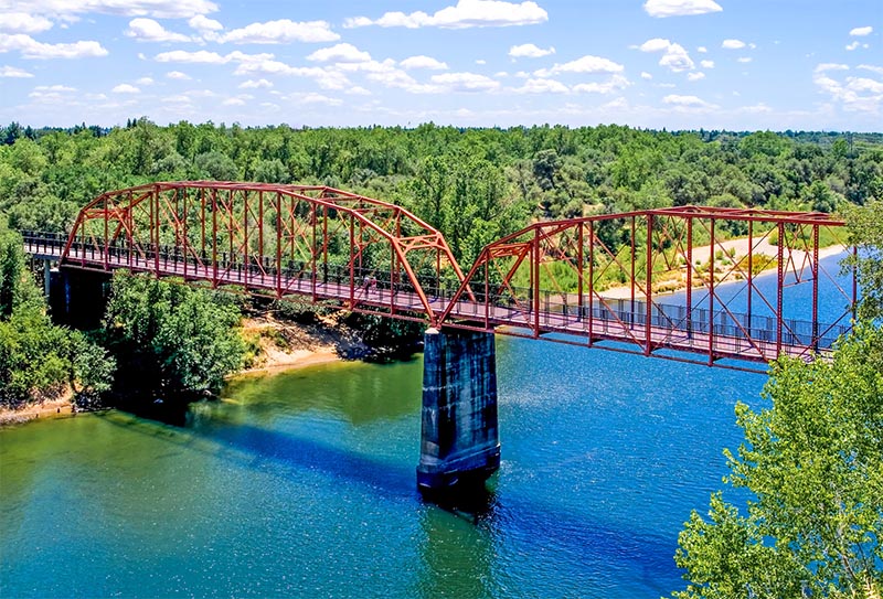 A large bridge suspended over a river with lots of trees surrounding it in Fair Oaks California