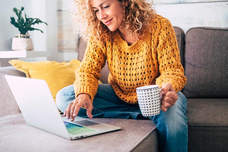 A woman sitting on the couch and searching for a rental home on her laptop