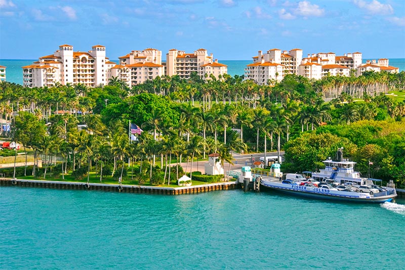 Condominium buildings in the distance above trees and a docked boat on Fisher Island Florida