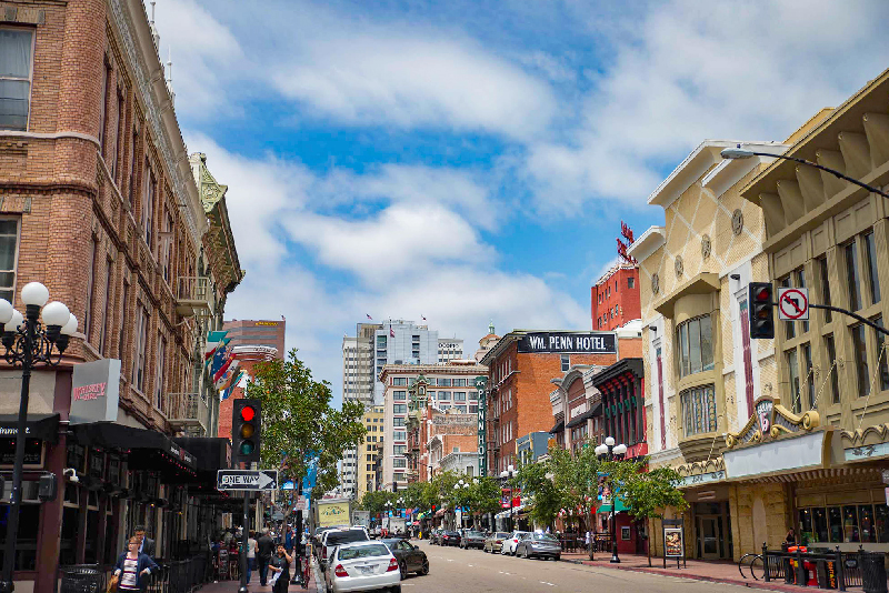 Looking down street with businesses and mid-rise buildings and blue sky.