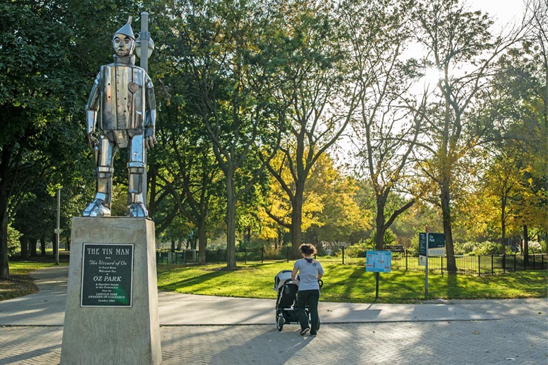 tin man statue in front of park with woman walking by