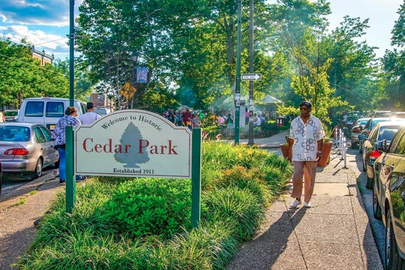 historic cedar park sign with recreational park in background and man walking on sidewalk