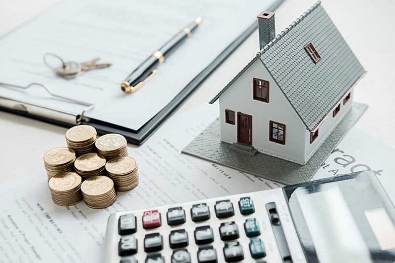 A model house, a calculator, a stack of coins, and a home loan on a clipboard