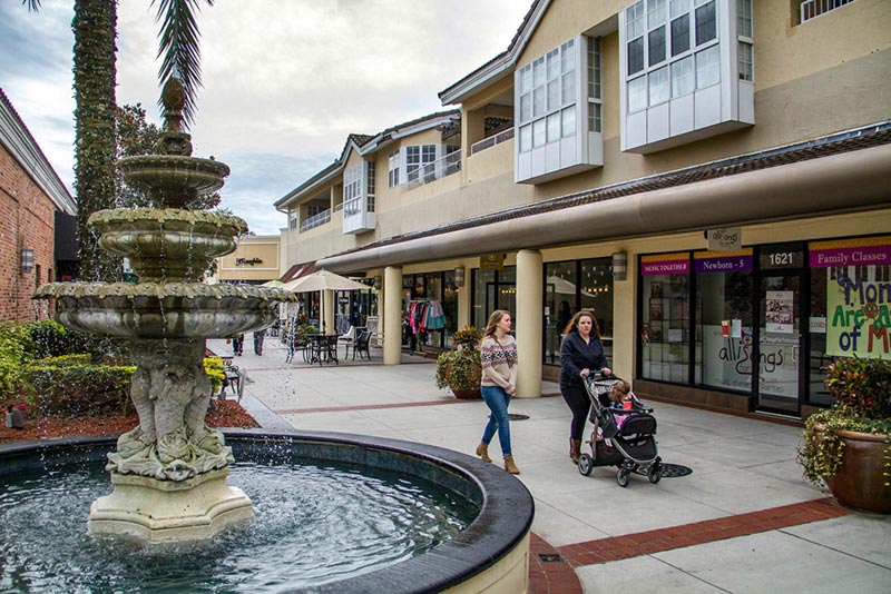 People walking around fountain in shopping plaza.