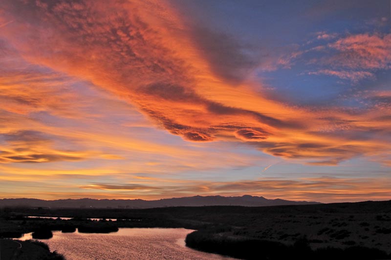 Aerial image of sunset reflecting on wetland landscape with mountain range in the background.