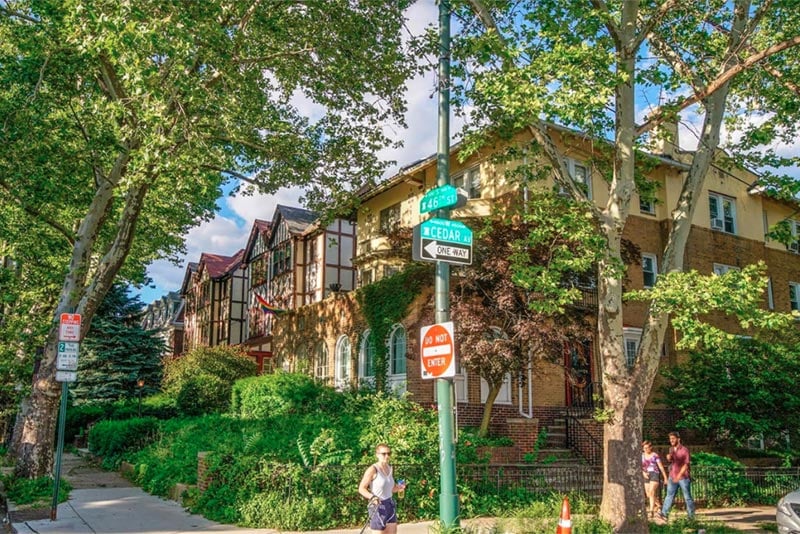 corner of neighborhood street with people walking by and various houses in the background