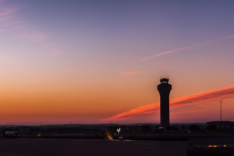 Sun setting on airport with control tower in view.