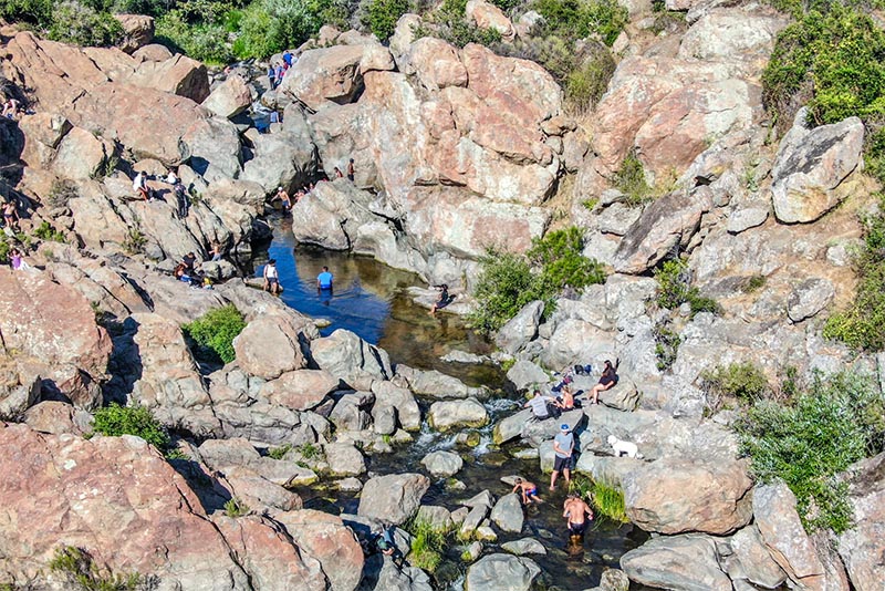 Hikers wading in the waters at Los Penasquitos Creek surrounded by large rocky cliffs.