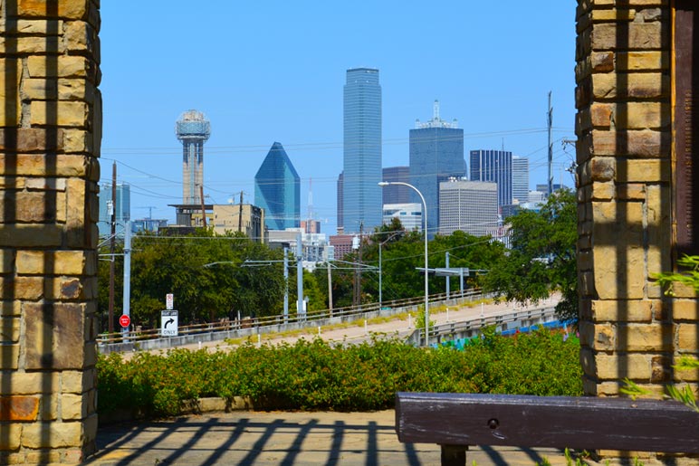 Downtown Dallas skyline framed in gazebo with bench.