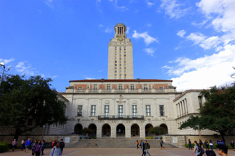 View of a University of Texas buildings with students and people in front on a sunny day.