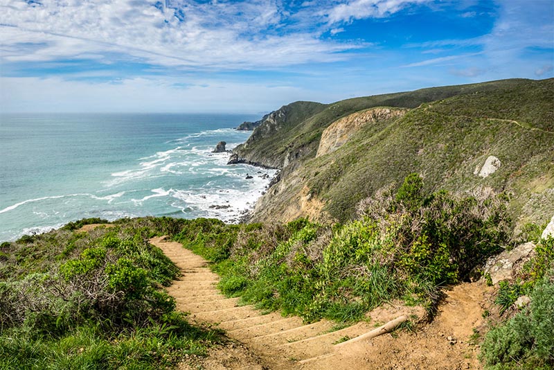 A hiking trail hugs a cliff going downward towards the beach and ocean in San Francisco