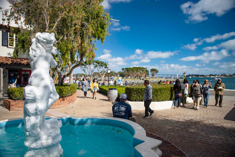 People walking along San Diego's marina district with closup of fountain and statue.