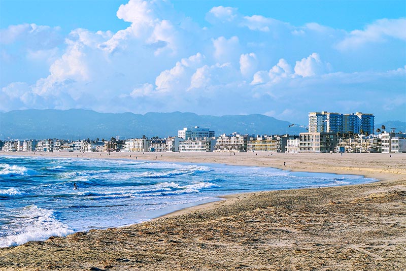 Marina del Rey beach with waves crashing in and buildings and mountains behind it