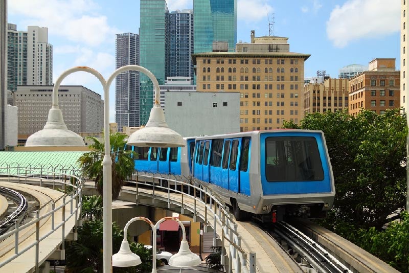 Blue Metro Rail train turning into station with Miami skyline in background.