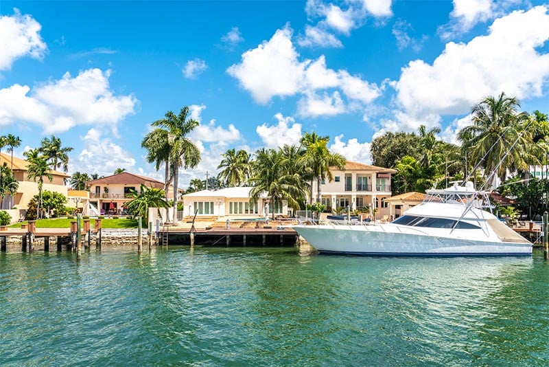 A luxury home with a yacht on the waterway in front of it in Miami Beach Florida