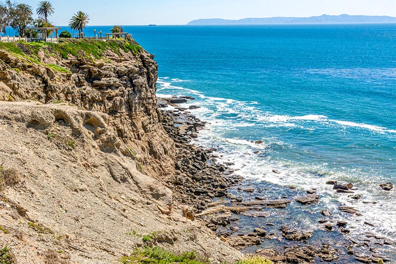 A tall cliff overlooks a rocky beachfront with ocean views.