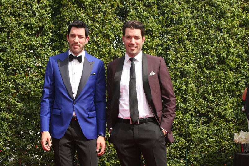 Drew and Jonathan Scott standing in front of a hedge. 