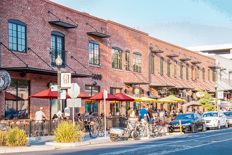 A large brick restaurant with many people walking along the patio and sidewalk in Sacramento