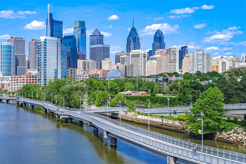 The skyline of Philadelphia with the Schuylkill River beside it, and a trail runs over the water and into the city